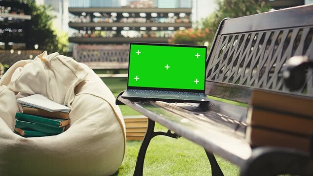 Green screen mockup on a laptop appears on a bench at a modern campus, offering an isolated editable screen for education and digital learning visuals.