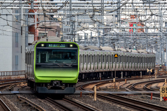 View of the E235 series Yamanote Line train arriving at Akihabara Station with overhead power lines and urban tracks in Chiyoda City, Tokyo, Japan.