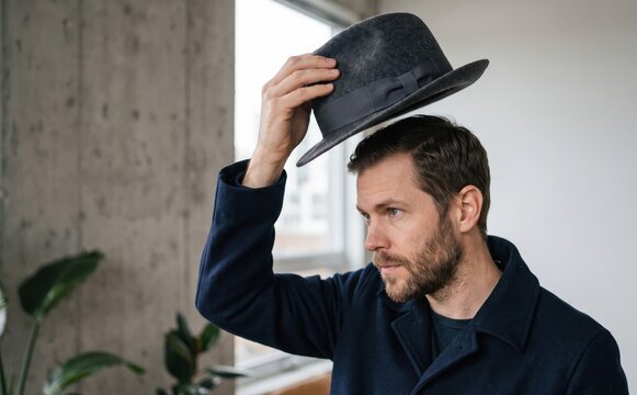 Middle-aged caucasian man tipping his fedora hat indoors, concept of politeness and greeting