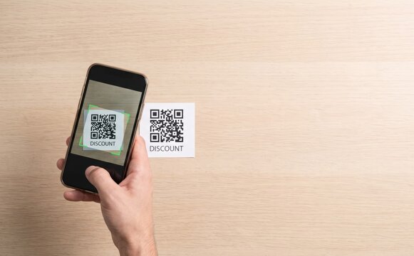 Smartphone scanning a discount QR code on a wooden table representing contactless shopping and promotional offers