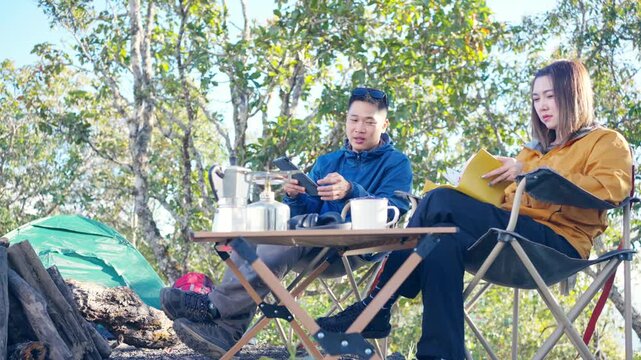 Asian man and woman remote working corporate business on digital tablet and smartphone while travel nature camping in forest with drinking coffee. Digital nomad workation outdoor active lifestyle