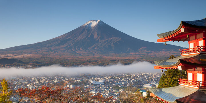 View of the iconic Chureito Pagoda with Mount Fuji in the background, framed by low-lying clouds and clear blue sky in Japan.