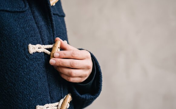 Close up of a young adult woman fastening a blue wool duffel coat with wooden toggle buttons