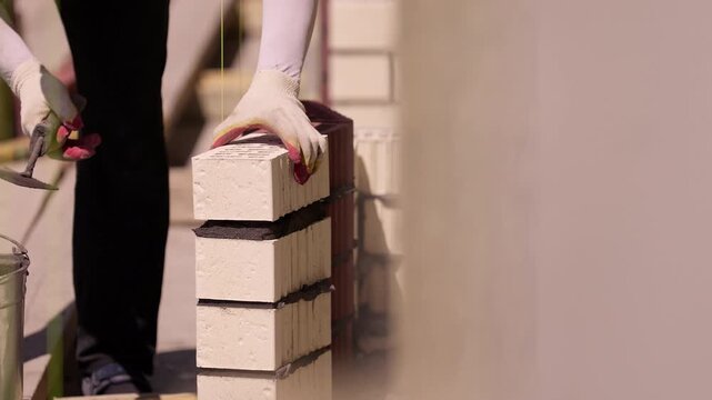 Worker placing ceramic brick on fresh mortar during wall construction close up