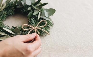 Fototapeta premium Woman making a Christmas wreath with pine branches and jute twine for holiday home decor