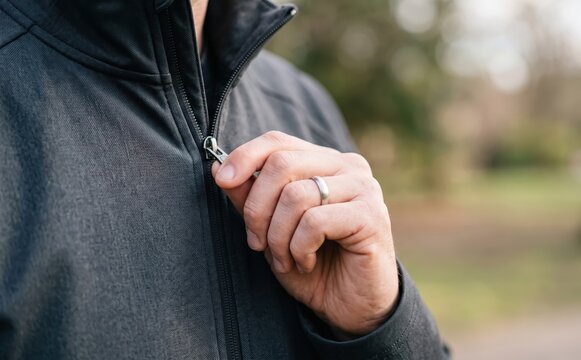 Man zipping up his black jacket outdoors representing warmth, fashion, and everyday apparel