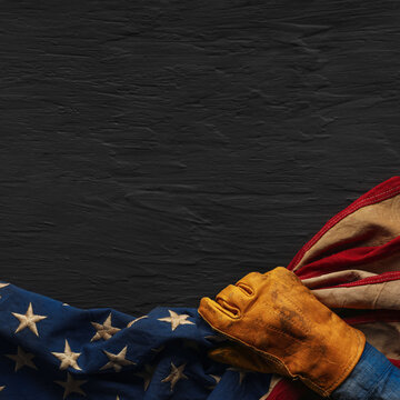 Work glove pulling the American flag with worn black background. Symbolic of hard working blue collar workers, pride in American manufacturing or products Made in USA, or to celebrate US Labor Day.