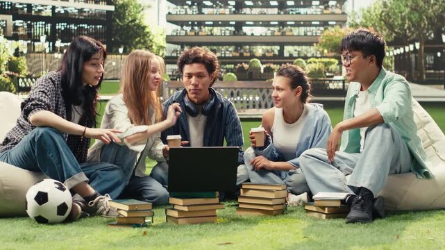 Diverse students check notes on a laptop with a stack of books during an outdoor campus study session, sharing ideas for a collaborative academic project, supporting research teamwork.