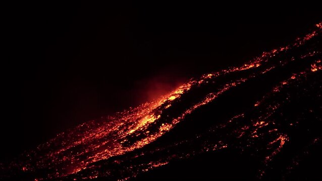 Bright molten lava spreads across the dark slope of Mount Etna during a night eruption in Sicily Italy creating glowing streams of volcanic rock surrounded by an intense fiery landscape