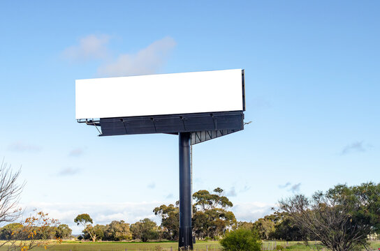 a large blank white billboard mockup set against a blue sky, standing beside an agricultural paddocks in regional Victoria, Australia.