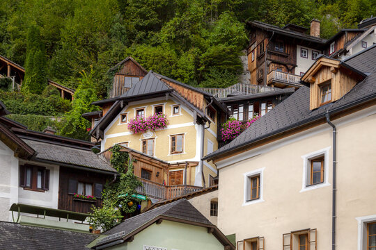 View of traditional alpine houses with flower-filled balconies, wooden facades, and steep roofs nestled against a lush green hillside in Hallstatt, Upper Austria, Austria.