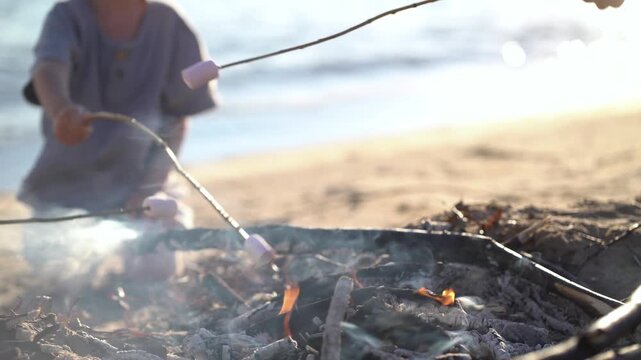 Kids roasting marshmallows over a beach campfire at sunset. Warm family outdoor moment with smoke, sand and ocean.