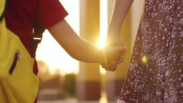 Mother and child holding hands, warm sunlight in the background, childhood innocence, summer day, loving bond, yellow backpack, floral dress, family support, close relationship, trust and care,