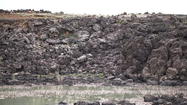 Basalt lava plain with calm lake water and dark volcanic rock reveals a rugged basin.
