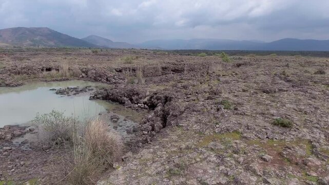 Aerial basalt lava plain with calm lake water and dark volcanic rock reveals a rugged basin.