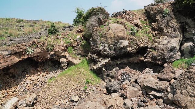 Basalt lava plain with porous volcanic rocks and sparse vegetation forms a harsh landscape.