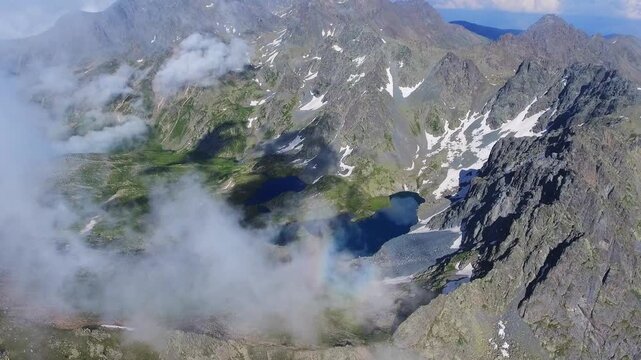 Aerial drone view of alpine tarn lake with rocky shore, green meadow, and mountain peaks.