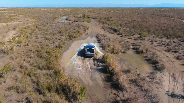 Aerial view of 4x4 safari SUV driving across flat plain on dusty dirt road adventure.