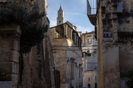 View of the historic stone architecture and narrow streets of the Sassi di Matera, with a church bell tower rising in the background in Matera, Basilicata, Italy.