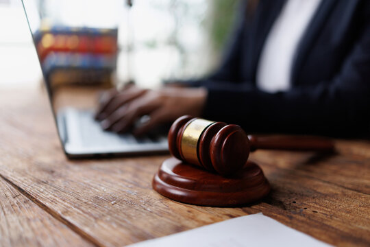 Gavel on a desk with a lawyer typing on a laptop, symbolizing online legal work, justice, and remote law services