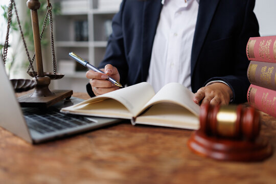 Lawyer reading law book and writing notes at desk with scales of justice and gavel, symbolizing legal services and counsel
