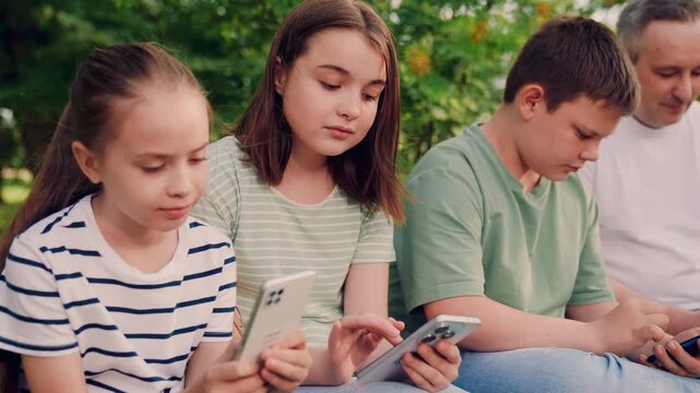 children and an adult sit outdoors, and chatting., adult and children using smartphones together, technology and childhood in a sunny backyard, screen time for children in the garden, kids browsing