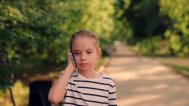 phone conversation with little girl outdoors, happy kid on phone during outdoor walk, little girl talking on phone in park, kid speaking on phone among green trees, youngster on mobile call in leafy