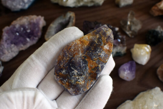 A hand in a white glove holds a purple fluorite against a background of gemstones