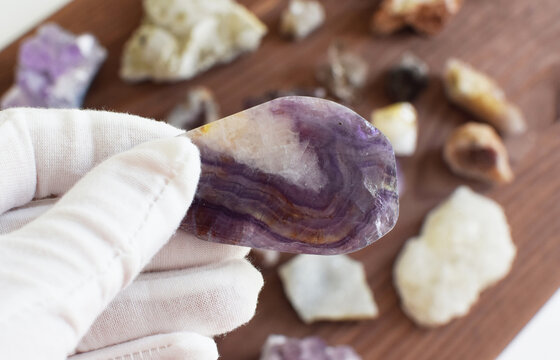A white-gloved hand holds a polished striped purple fluorite against a background of gemstones