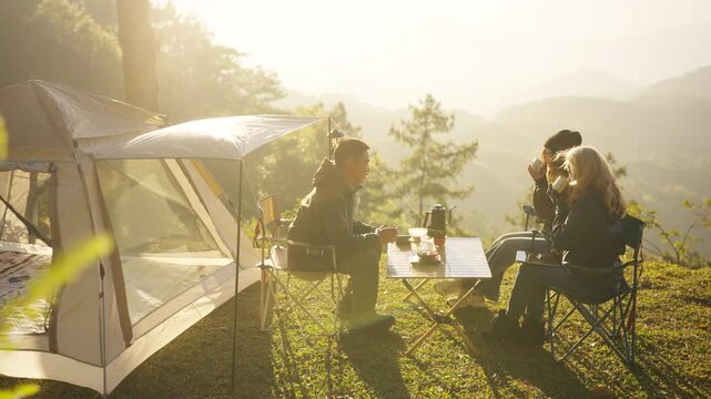 Group of Asian adult friends relaxing drinking brewed coffee together beside tent at mountain campsite in morning. people traveler enjoy outdoor active lifestyle travel nature on holiday vacation