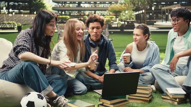 Diverse students check notes on a laptop with a stack of books during an outdoor campus study session, sharing ideas for a collaborative academic project, supporting research teamwork.