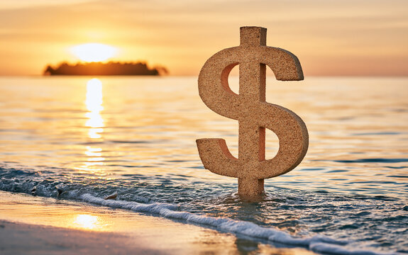 A textured dollar sign symbol stands upright on wet sand near the ocean shoreline during a warm golden sunset with gentle waves rolling in.