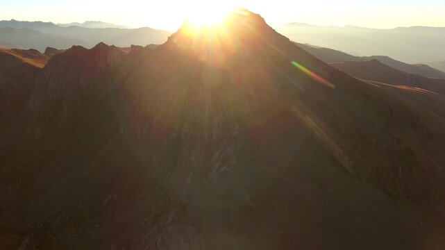 Aerial sunrise over imposing mountain peak with slanting sunbeams, epic horizon atmosphere.