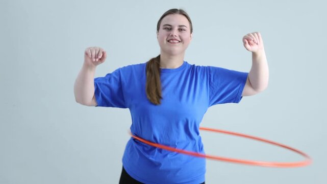 Overweight woman exercising with hula hoop on light grey background