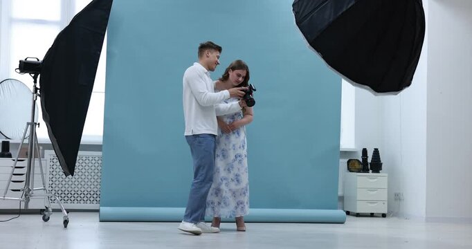 Young overweight woman in dress posing for photographer with camera against light blue background in studio. Plus size model