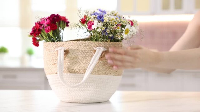 Woman with wildflowers in bag at white table indoors, closeup