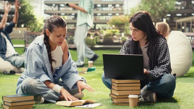 Diverse classmates sit on a campus lawn and collaborate over a laptop, discussing coursework and taking notes for exam preparation during outdoor group study.