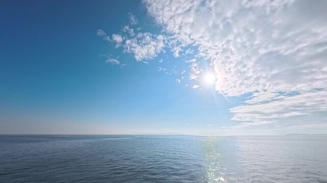 Cinematic real-time wide angle video of radiant sun flare breaking through clouds over glowing ocean
