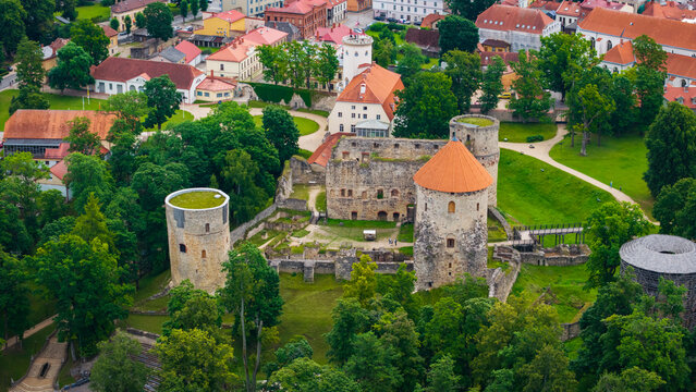Aerial view of Cesis Castle surrounded by lush green trees, historic stone walls, and orange-tiled roofs in the old town of Cesis, Cesis Municipality, Latvia.
