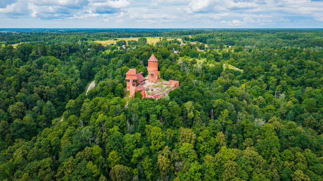 Aerial view of Turaida Castle surrounded by dense green forests under a blue sky with clouds in Sigulda, Siguldas novads, Latvia.