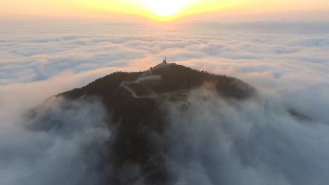Aerial mosque and minaret above sea of clouds at sunrise during Ramadan, serene prayer scene.