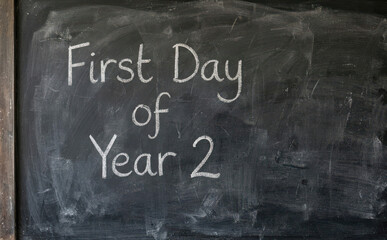 Fototapeta premium First Day of Year 2 written in white chalk on a dark blackboard representing back to school and education concepts for students