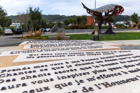 Engraved stone slabs featuring French poetic text stand beside a colorful sculptural canopy in Pukeahu National War Memorial Park, Wellington, New Zealand
