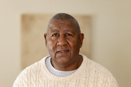 Mature African American man posing facing camera in studio wearing cream sweater blurred canvas