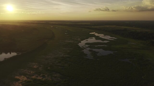 Aerial drone footage of Ujan Gram Bill in Kushtia, Bangladesh, showing open wetland areas, scattered water channels, vegetation, and surrounding agricultural fields during sunset.