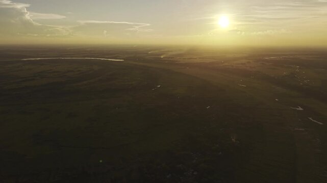 Aerial drone view of Ujan Gram Bill in Kushtia, Bangladesh, showing the expansive rural wetland landscape, open fields, scattered water bodies, and surrounding countryside under a setting sun.
