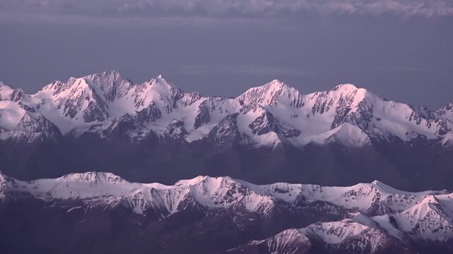 Switzerland Alps snowy peaks shine above clouds and winter ridges in slanting sunlight.