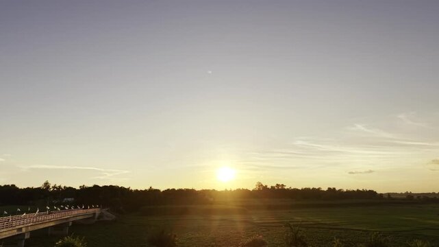 Aerial view of the open Ujan Gram Bill landscape in Kushtia, Bangladesh, featuring expansive fields, rural vegetation, a bridge, and the setting sun along the horizon.