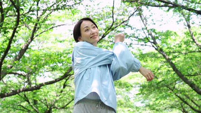 新緑の木々の下で腕を伸ばしてストレッチする女性