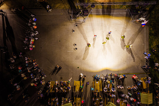 Aerial view of an outdoor evening event with people dancing under bright stage lights, surrounded by tables and spectators in Fuzine, Primorje-Gorski Kotar, Croatia.